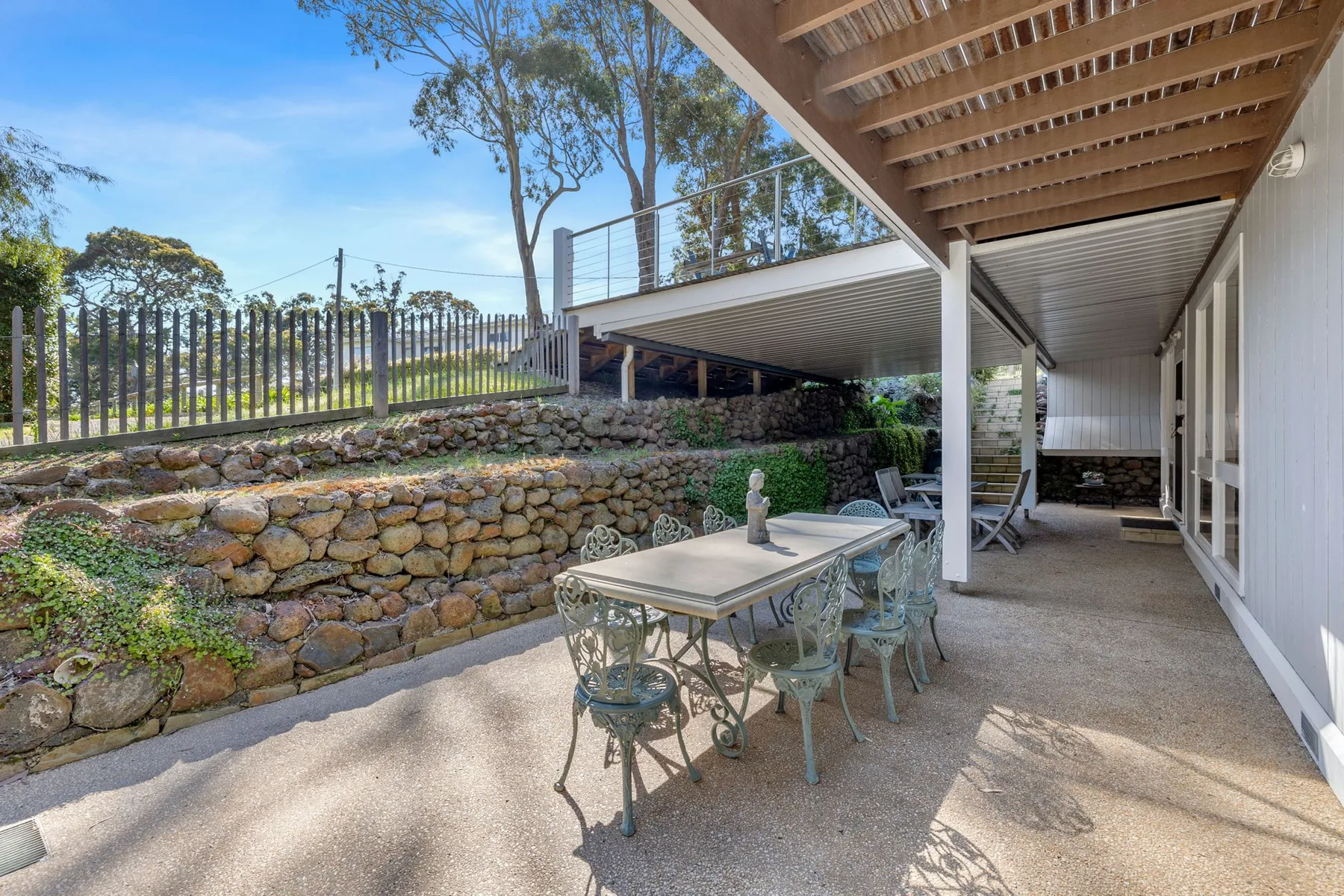 Covered patio with outdoor seating beside a stone retaining wall.