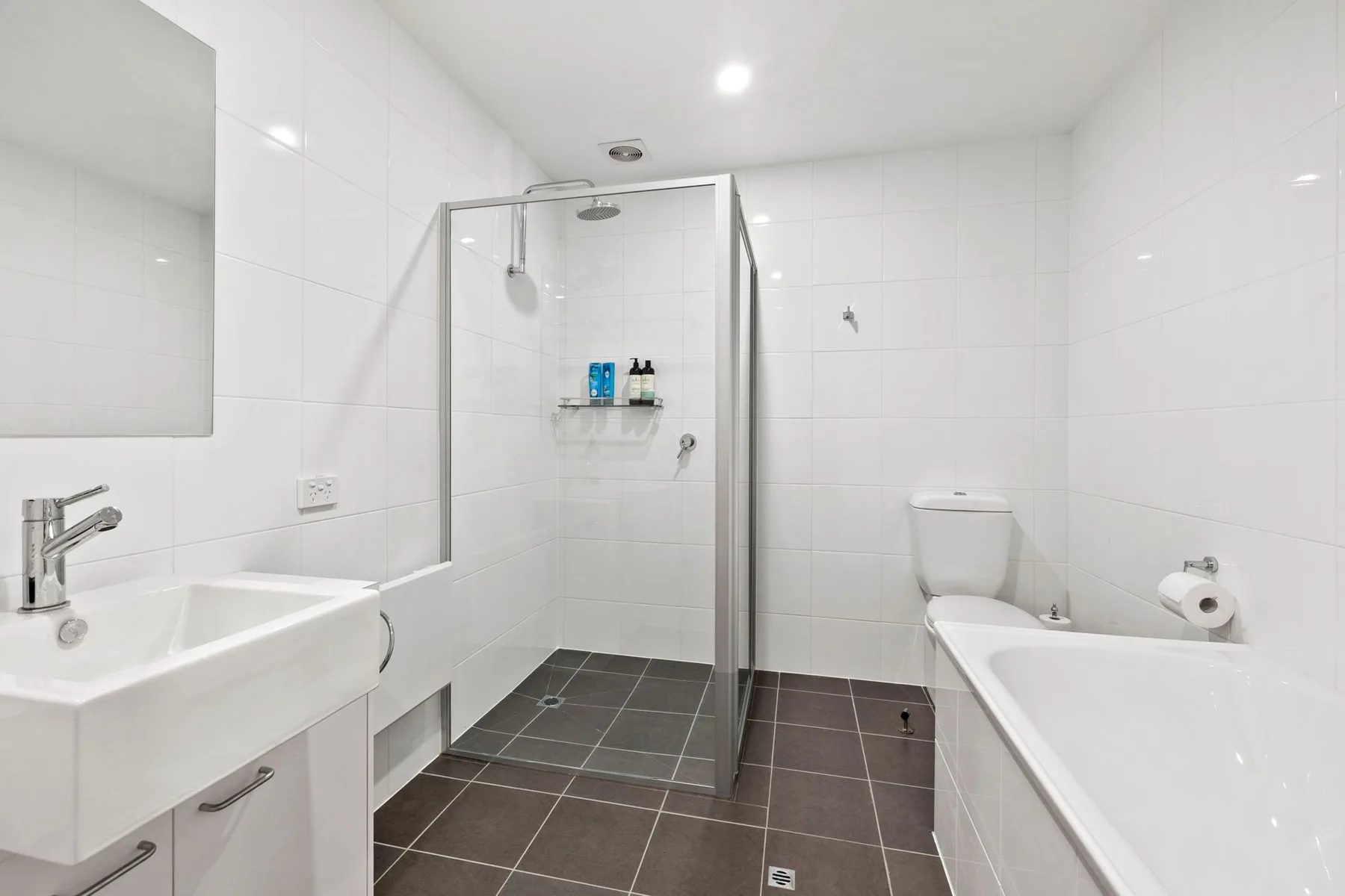 A tiled bathroom with a glass shower, bathtub, and sink.