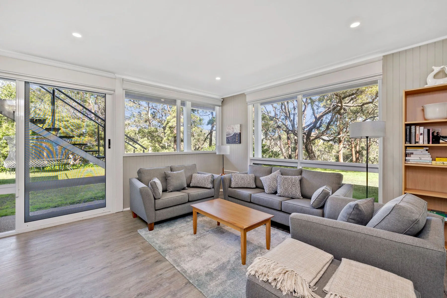 A bright living room with sectional seating and large windows overlooking trees.