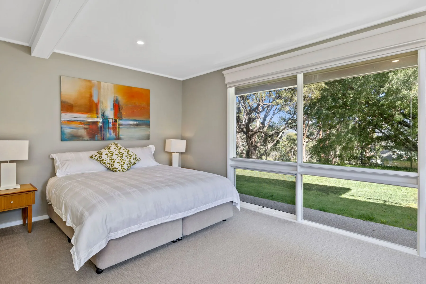 A bedroom with a bed beside large windows overlooking a garden.
