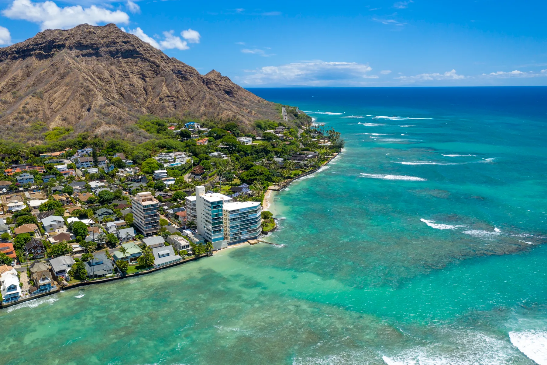 Aerial view of a coastal neighborhood beside turquoise water and a rugged mountain.