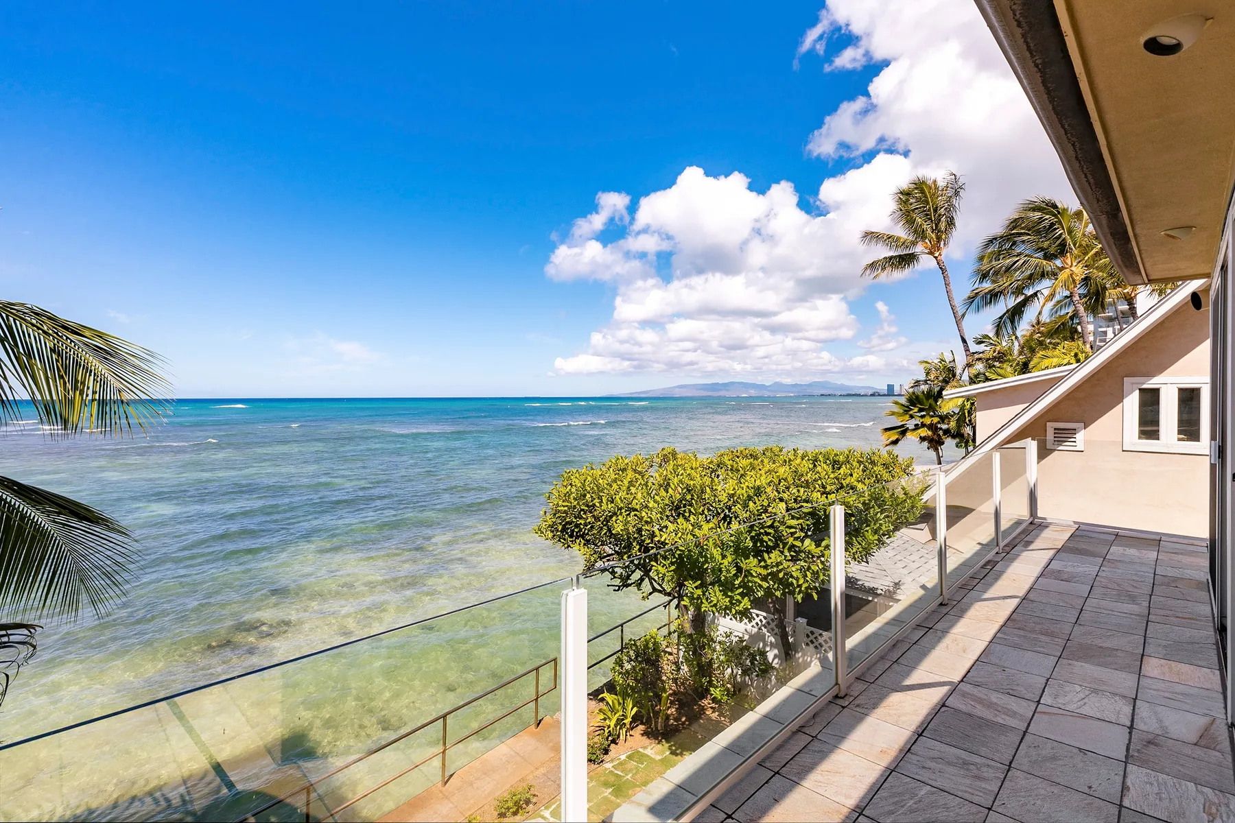 A seaside terrace overlooks clear water, with palm trees along the shore.