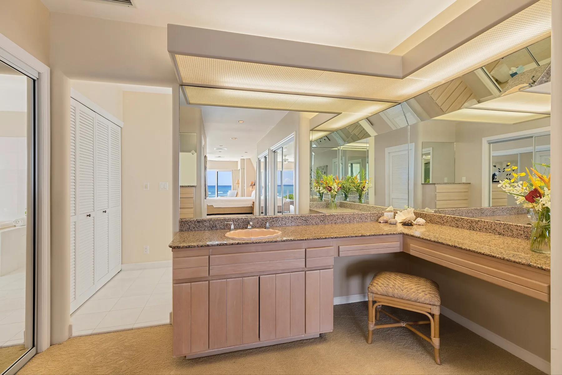 A vanity area with a long counter, large mirror, and woven seat.