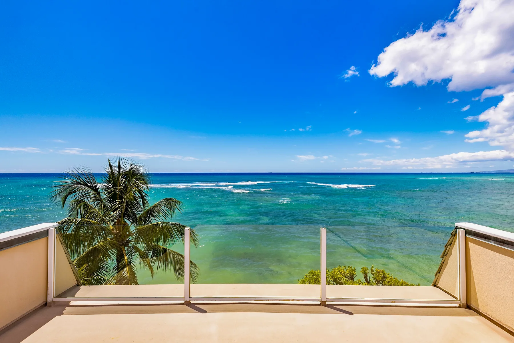 A balcony overlooks turquoise ocean water beneath a bright blue sky.