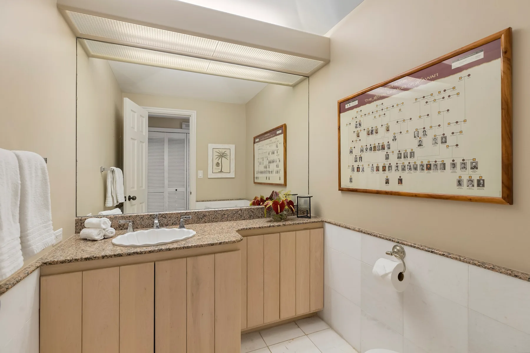 A bathroom with a long vanity, sink, and framed wall chart.