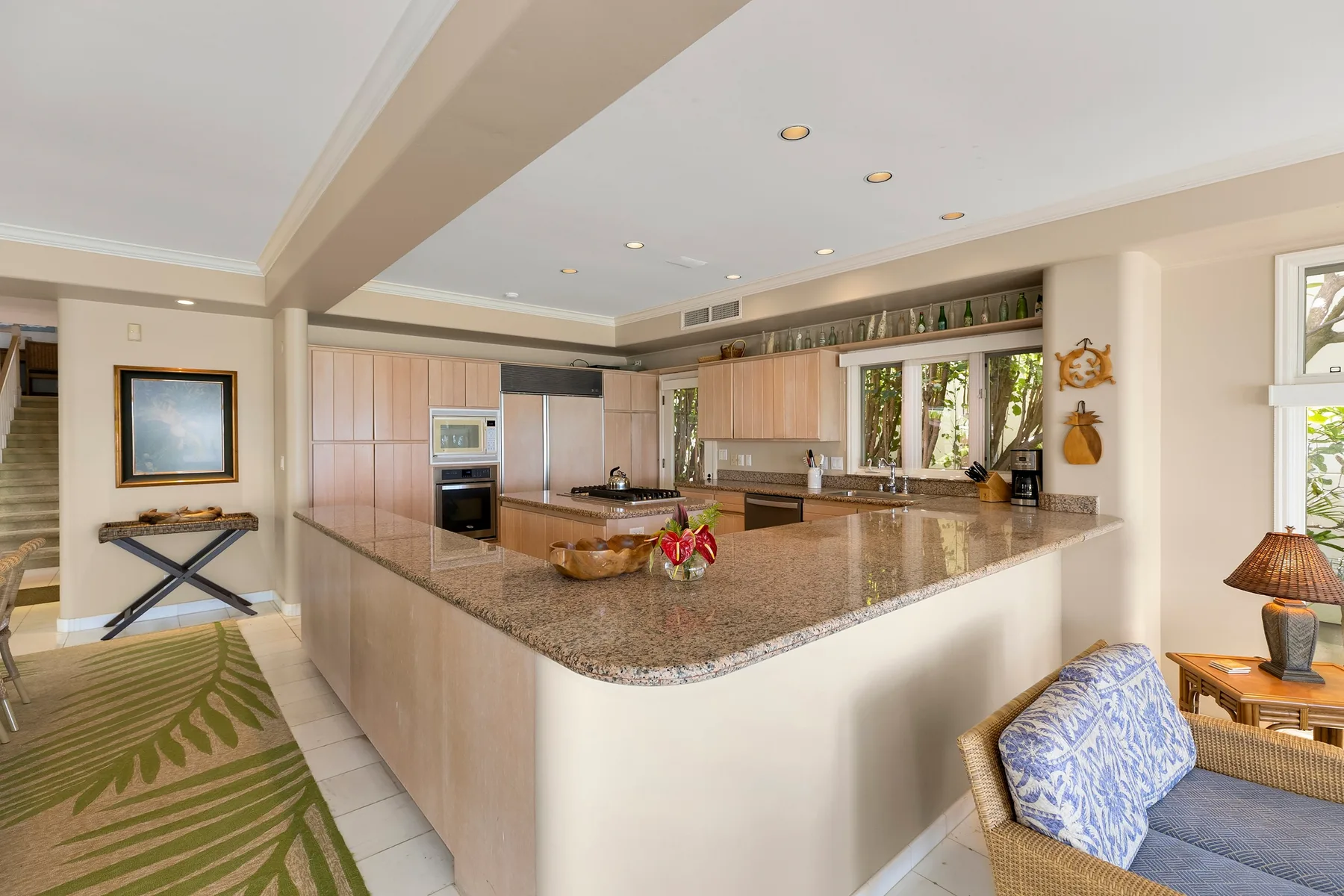 A bright open kitchen with a broad stone countertop and light wood cabinets.