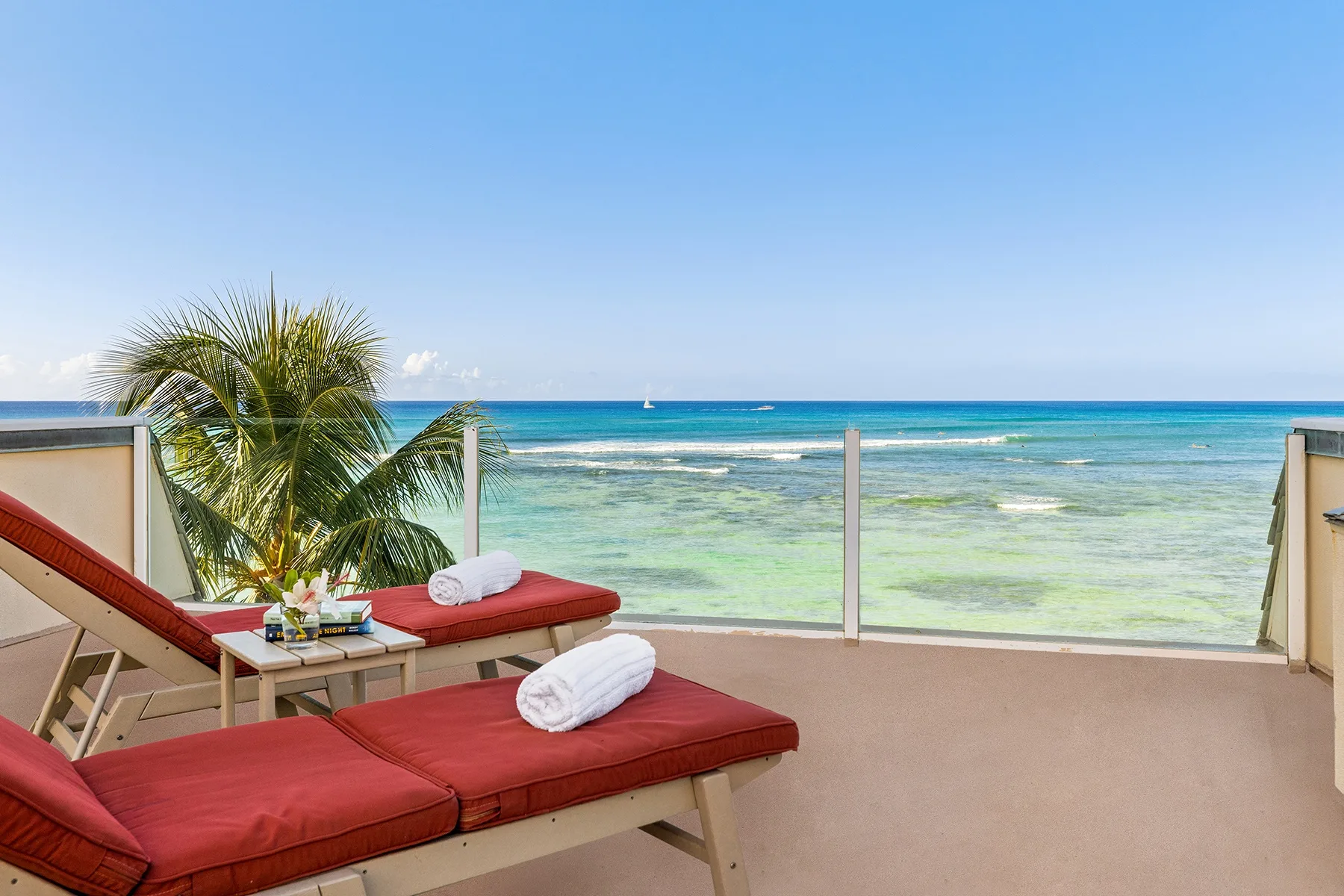 A seaside terrace with red cushioned loungers overlooking turquoise water.