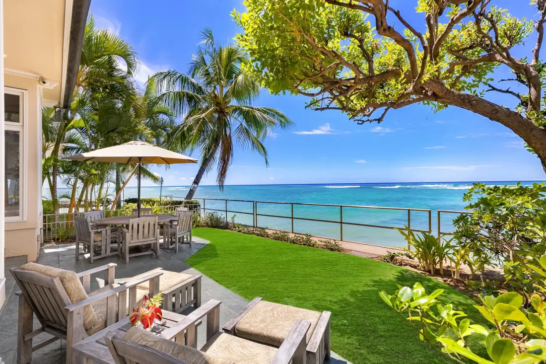 Un patio junto al mar da al agua turquesa, con asientos al aire libre y palmeras.