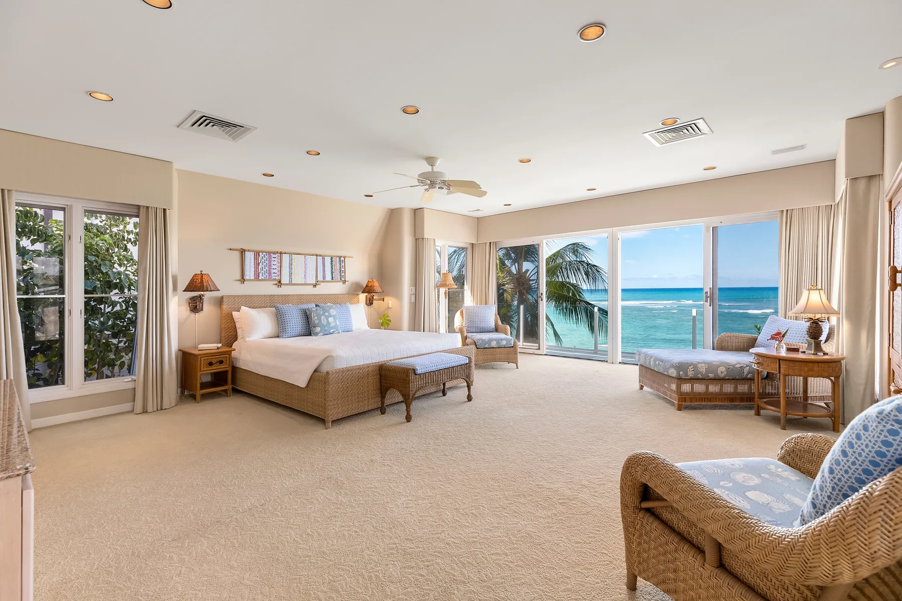 A bright bedroom with a bed and seating facing a large window overlooking the ocean.