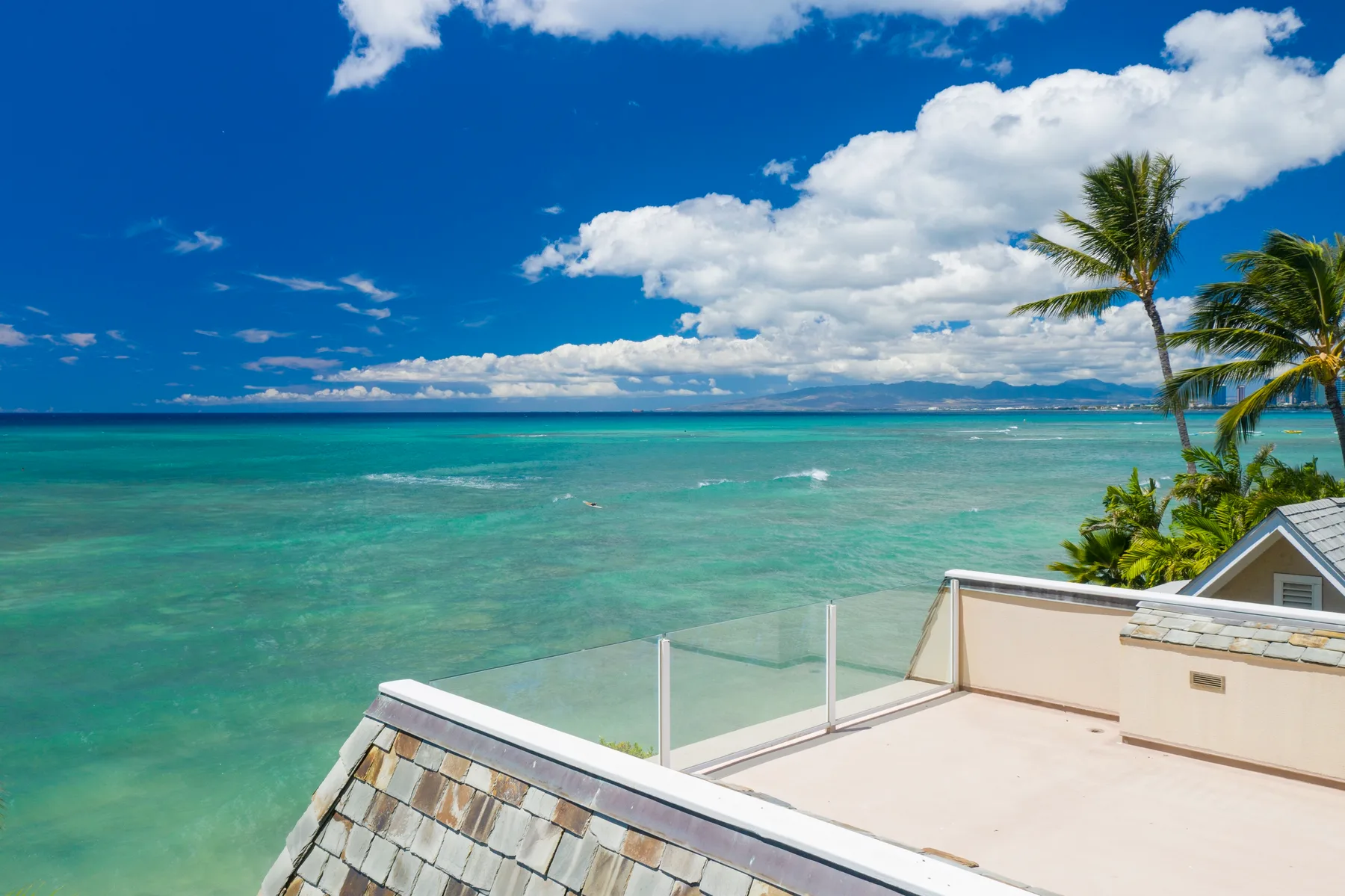A rooftop terrace overlooks turquoise ocean water and palm trees.