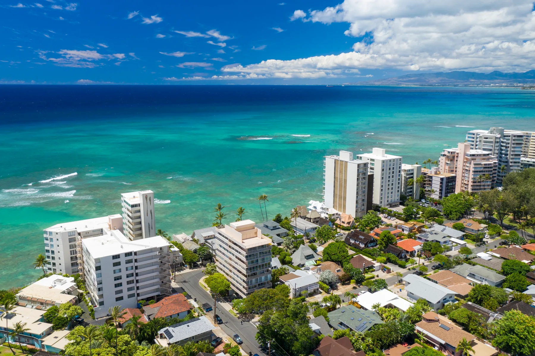 Aerial view of coastal buildings beside turquoise ocean water.