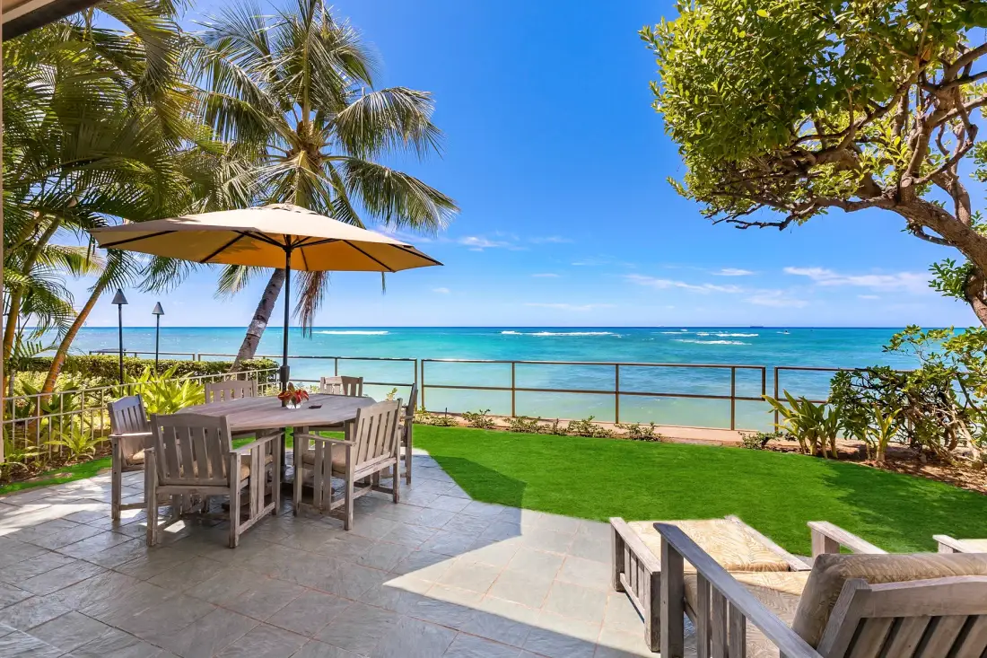 An outdoor dining area overlooks a grassy lawn and the ocean.