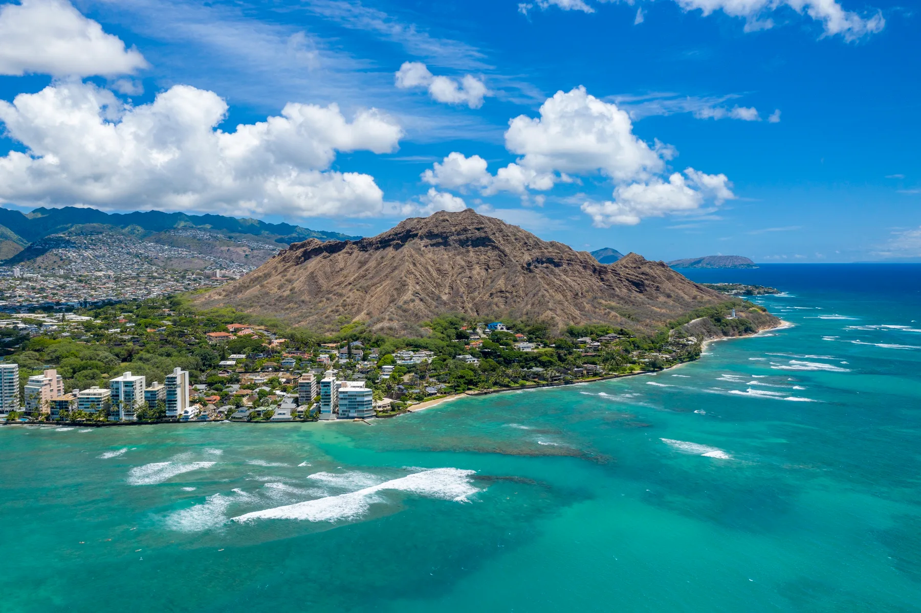 A coastal city sits beside turquoise water, with a rugged mountain rising behind it.