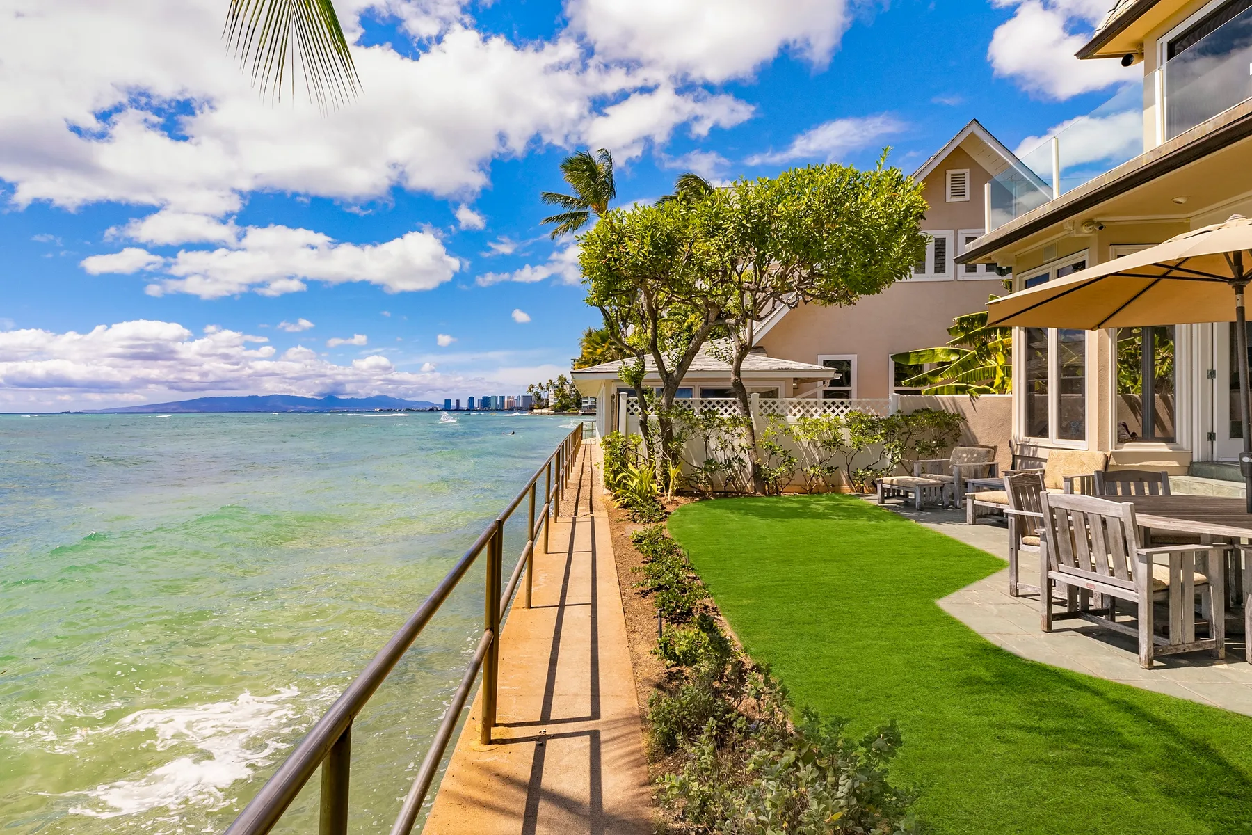 A waterfront patio and lawn overlook the water beside a tree-lined walkway.
