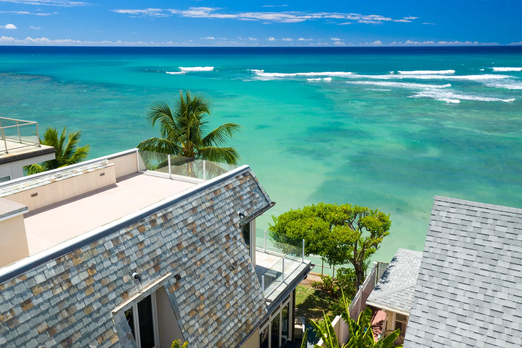 Aerial view of coastal buildings beside a turquoise ocean with breaking waves.