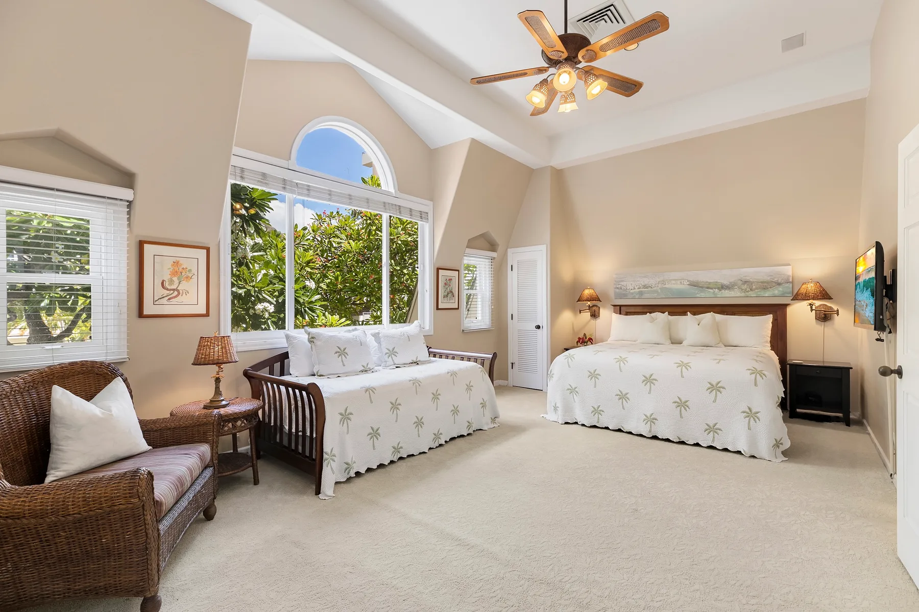 A bright bedroom with a large bed, seating, and tall windows overlooking greenery.