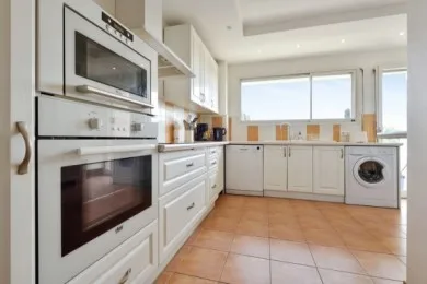 A bright kitchen with white cabinets, built-in appliances, and a washing machine.