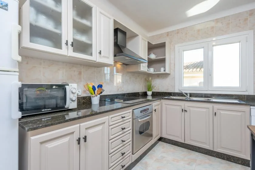 Una cocina luminosa con gabinetes blancos, encimeras oscuras y una ventana.