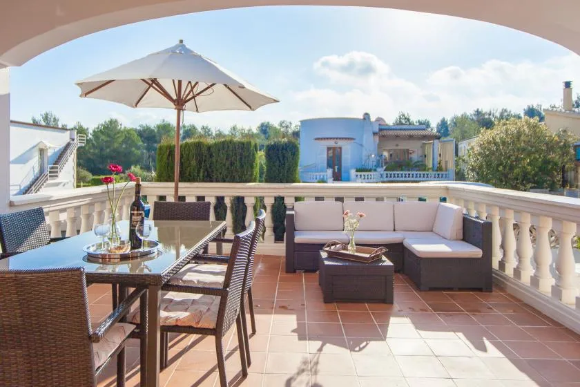 Una terraza con suelo de baldosas tiene una zona de estar al aire libre y una gran sombrilla.