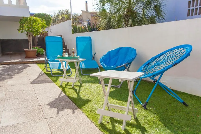 Un patio al aire libre con asientos azules y pequeñas mesas blancas junto a una pared blanca.