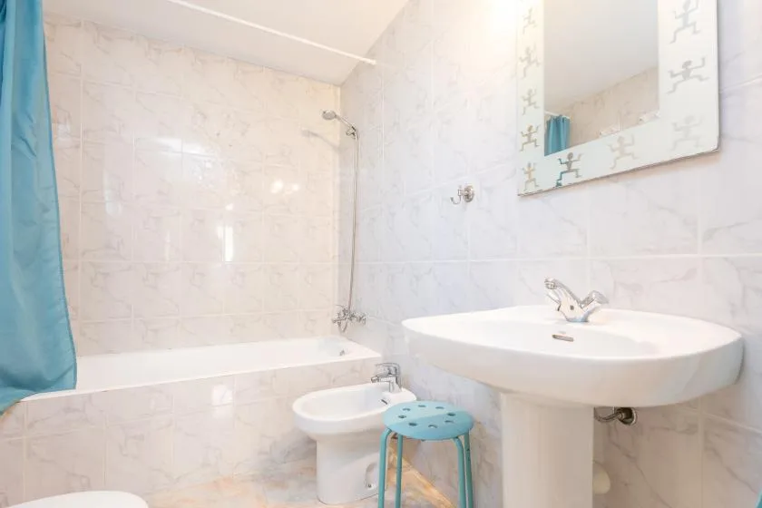 Un baño alicatado con bañera, lavabo con pedestal y cortina de ducha azul.