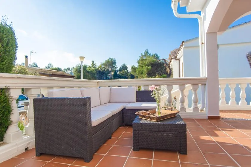 Una terraza exterior con suelo de baldosas, asientos acolchados y una mesa baja.