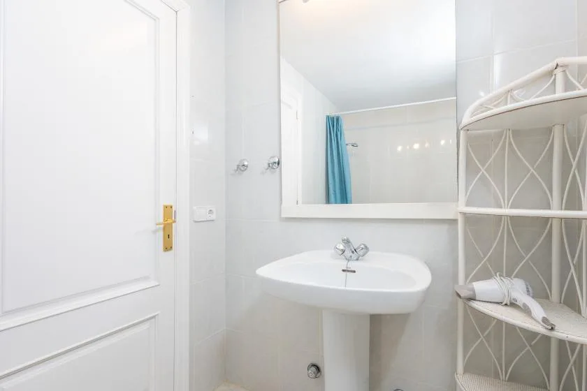 Un baño luminoso con un lavabo de pared y un espejo grande.