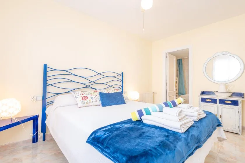 Un dormitorio con una cama blanca, ropa de cama azul y un cabecero metálico azul.