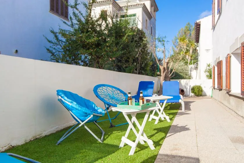 Una zona de estar al aire libre con sillas azules y una mesa pequeña sobre césped artificial.