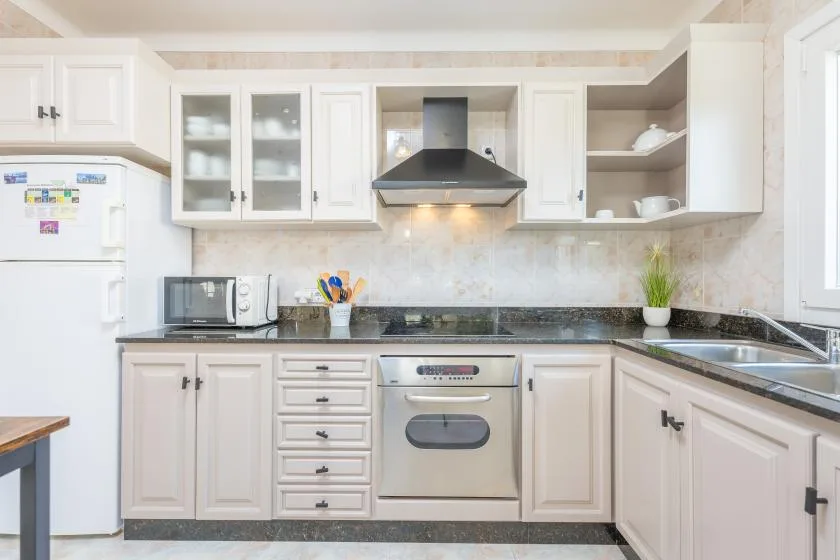 Una cocina luminosa con gabinetes blancos, encimeras oscuras y electrodomésticos de acero inoxidable.