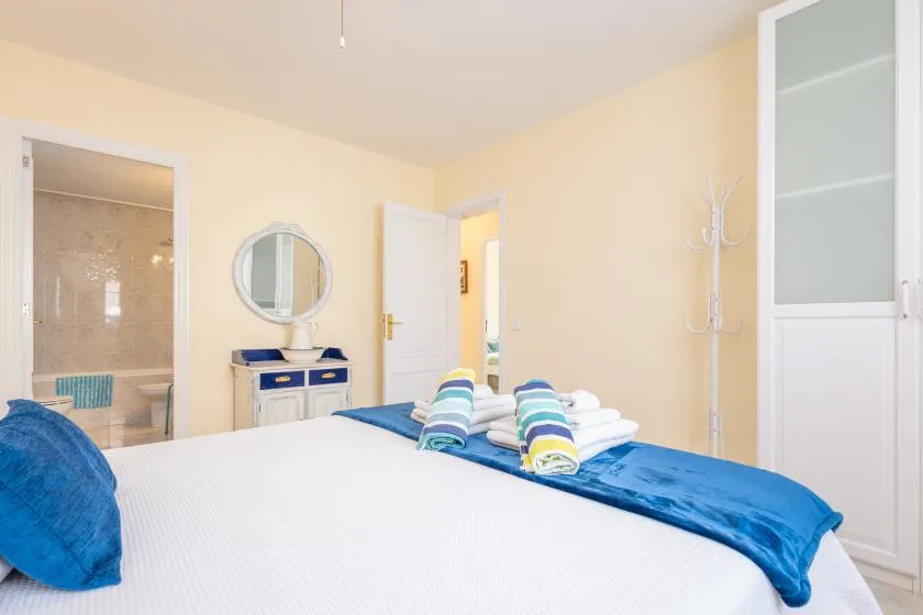 Un dormitorio luminoso con una cama y una puerta abierta hacia un baño.