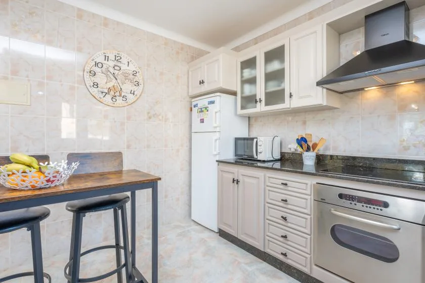 Una cocina luminosa con gabinetes blancos, refrigerador y una pequeña barra para comer.