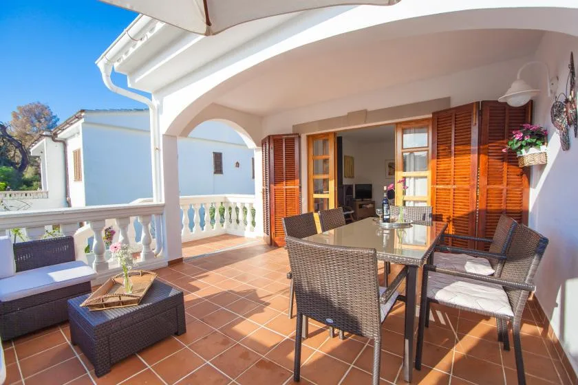 Una terraza cubierta con asientos al aire libre y una mesa junto a contraventanas abiertas.