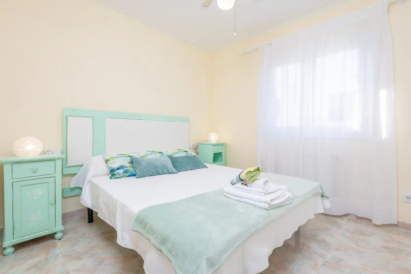 Un dormitorio con una cama vestida de blanco y verde menta junto a una ventana luminosa.