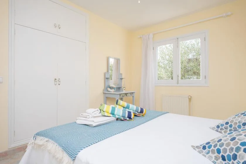 Un dormitorio luminoso con una cama bien hecha y una ventana con vistas a la vegetación.