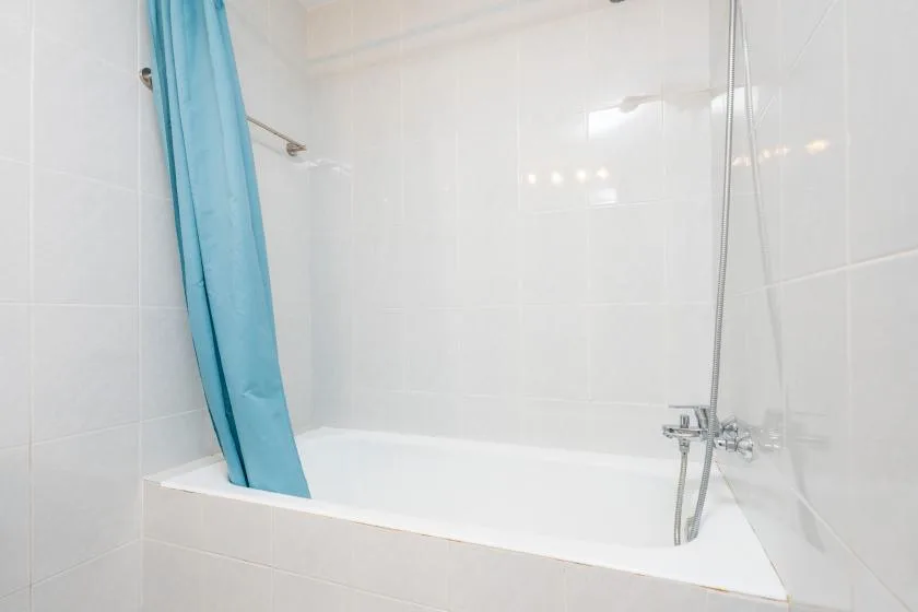 Una bañera blanca con una cortina de ducha azul y accesorios de ducha en la pared.