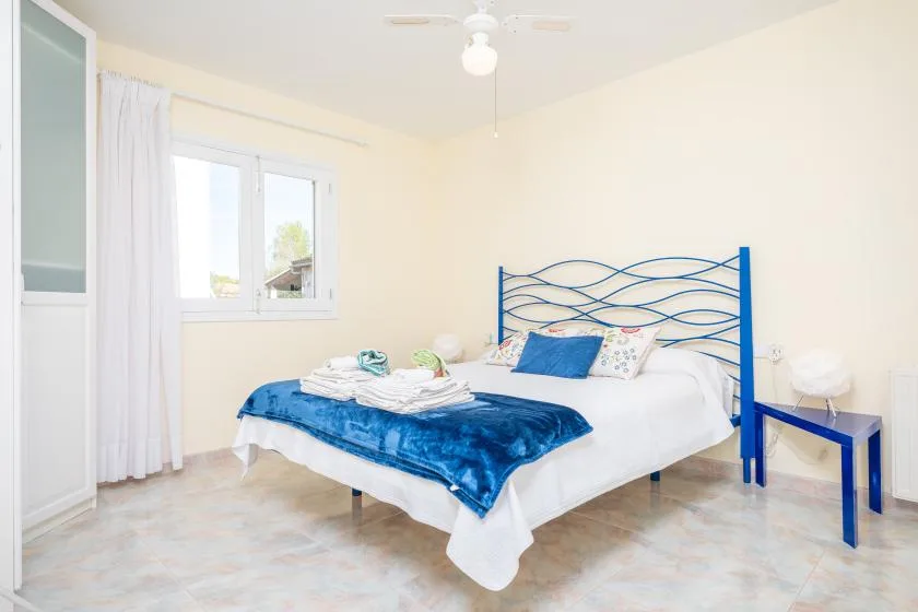 Un dormitorio luminoso con una cama cubierta con ropa de cama azul junto a una ventana.