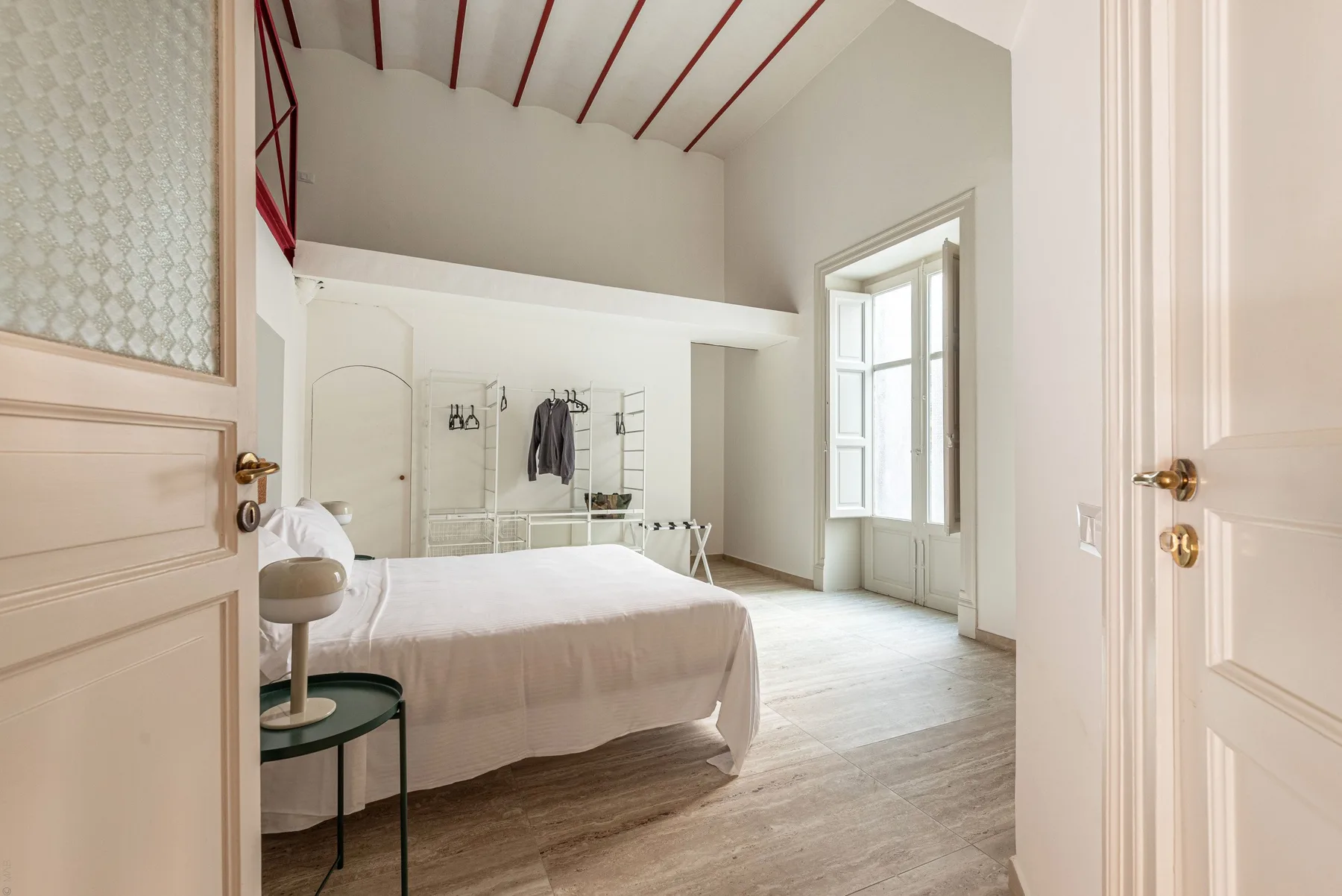 A bright bedroom with a bed, open wardrobe rack, and tall windows.