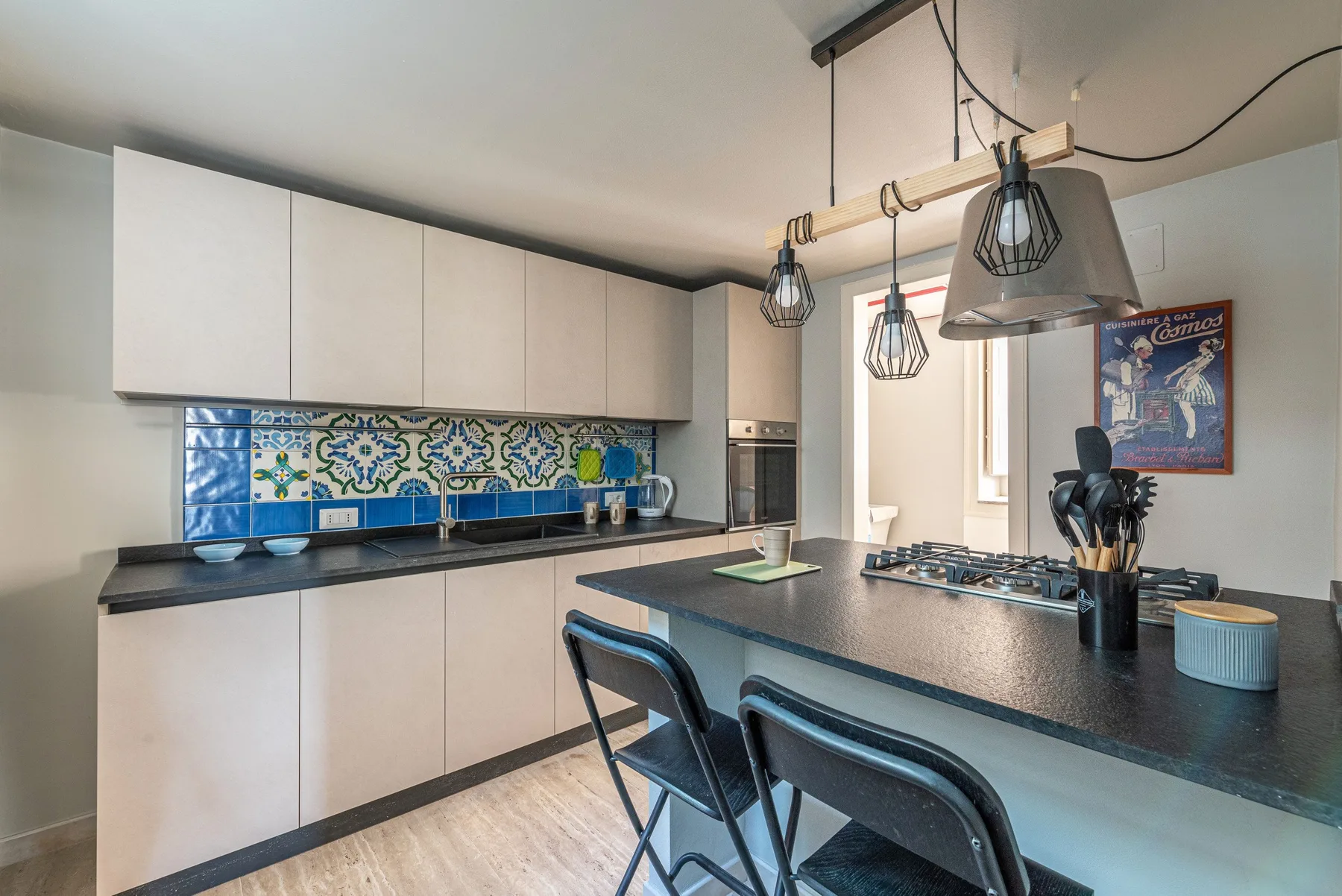 Una cocina moderna con una larga encimera, un salpicadero de azulejos coloridos y lámparas colgantes.