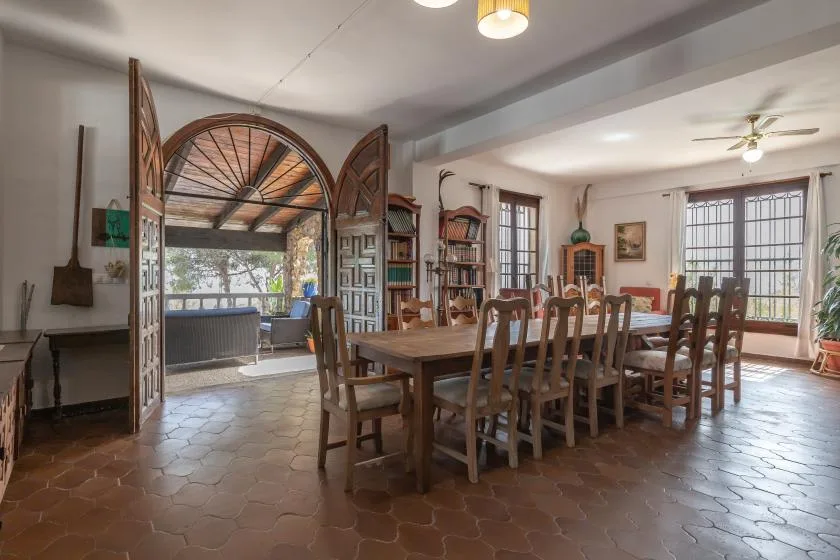A dining room with a long wooden table and an arched opening to a bright sitting area.