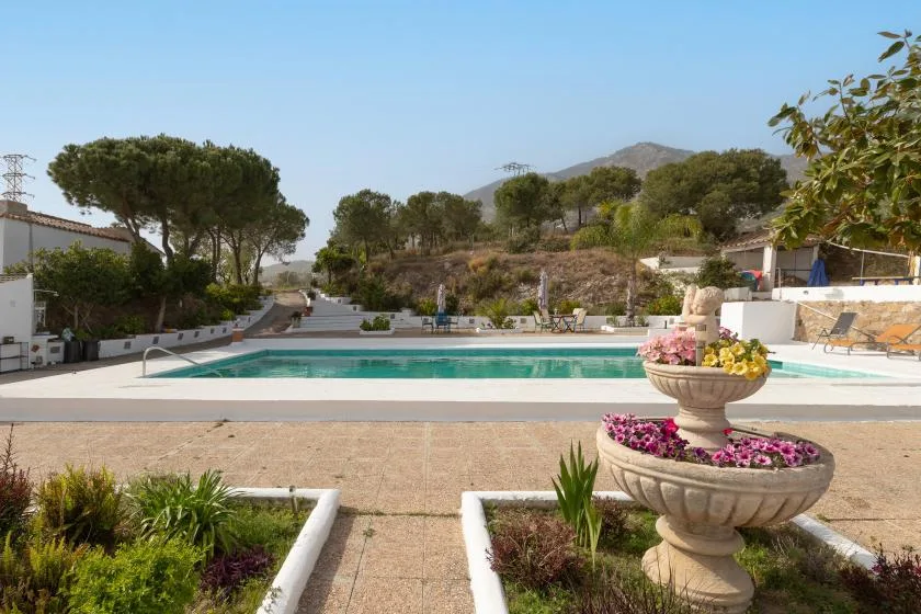 An outdoor swimming pool sits beside a landscaped garden and flower-filled stone fountain.