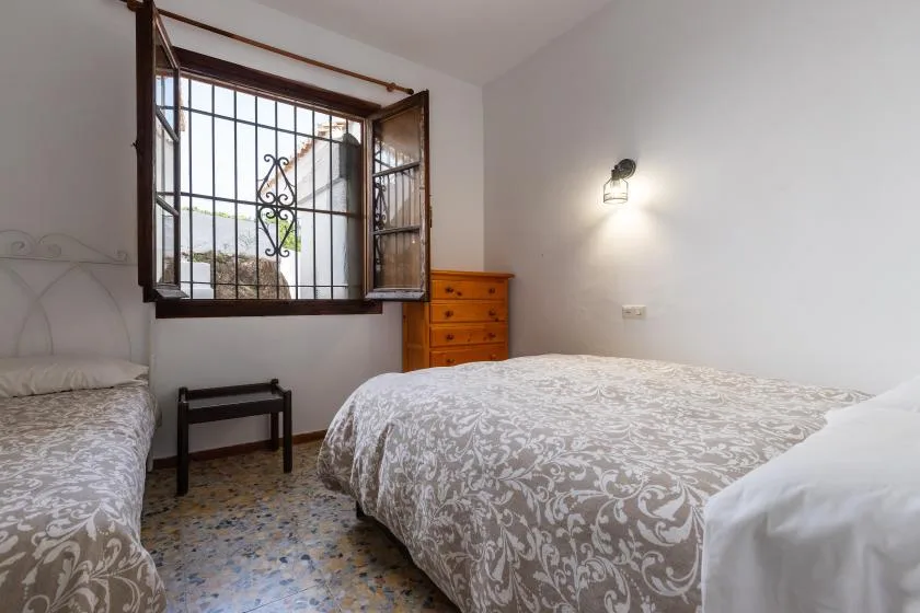 A bedroom with two beds, a barred window, and a wooden dresser.