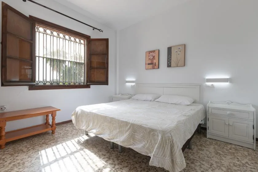 A bedroom with a bed, a barred window, and a bedside cabinet.