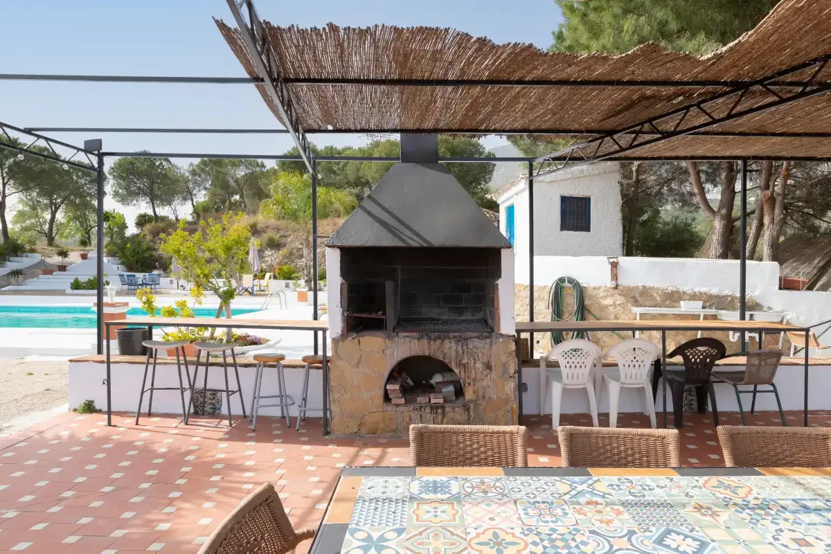 A tiled outdoor patio has a built-in barbecue, seating, and a shaded dining area.