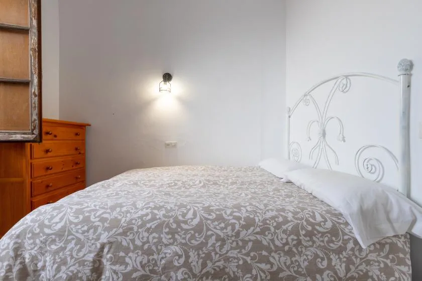 A bedroom with a patterned bedspread and a wooden chest of drawers.