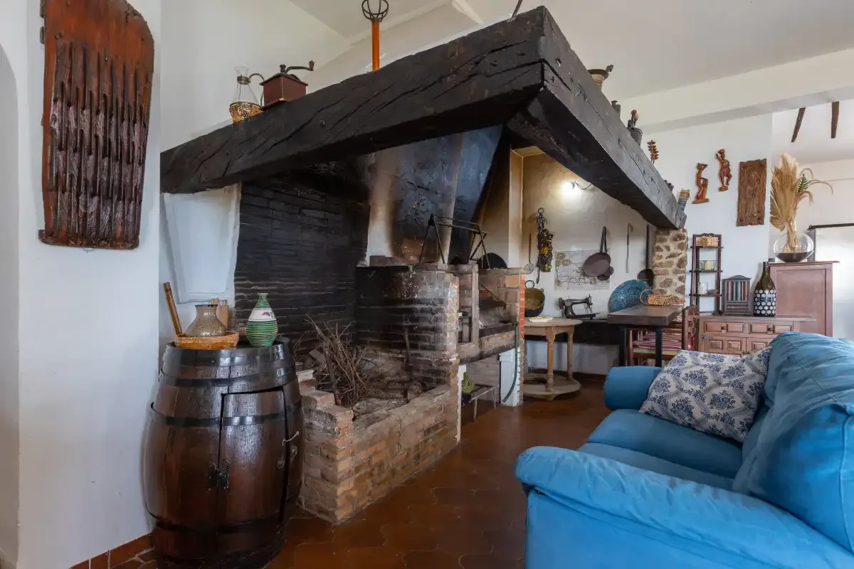 A living room with blue seating beside a large rustic fireplace.
