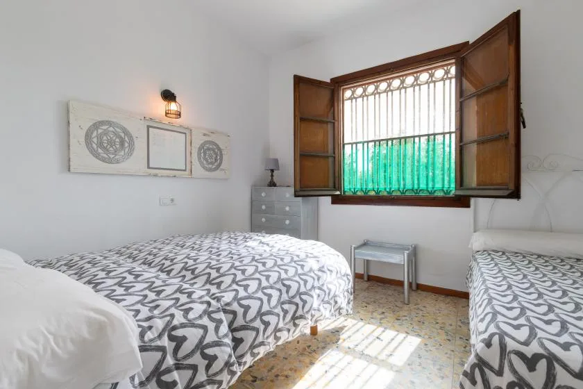 A bright bedroom with patterned beds and an open window with green curtains.
