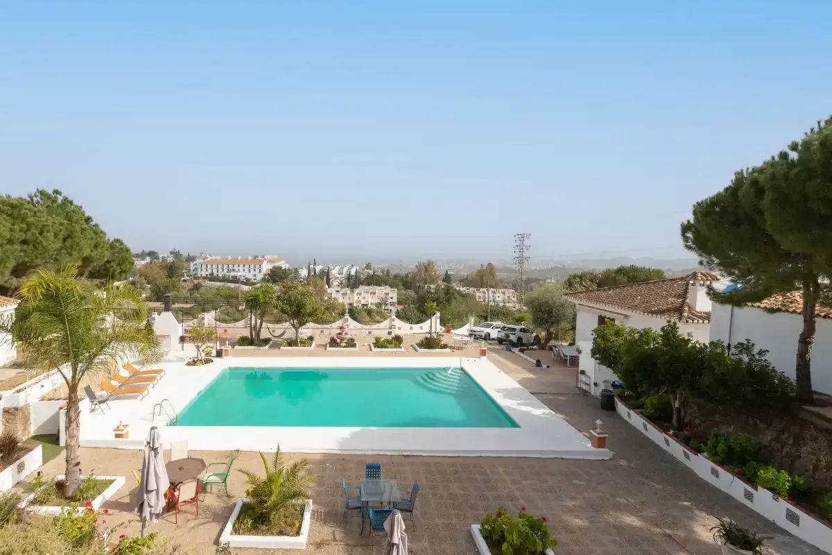 An outdoor swimming pool is surrounded by lounge seating and landscaped grounds.