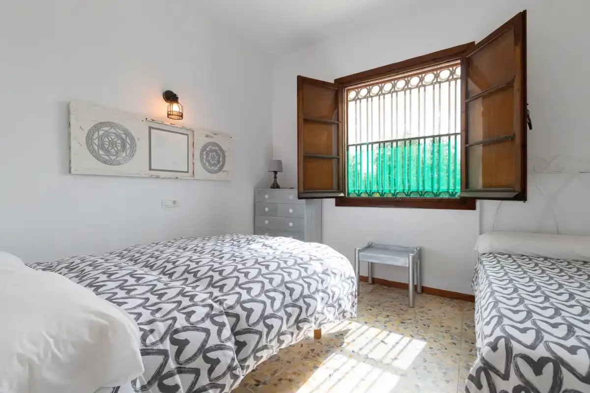 A bedroom with two beds, patterned bedding, and an open window.