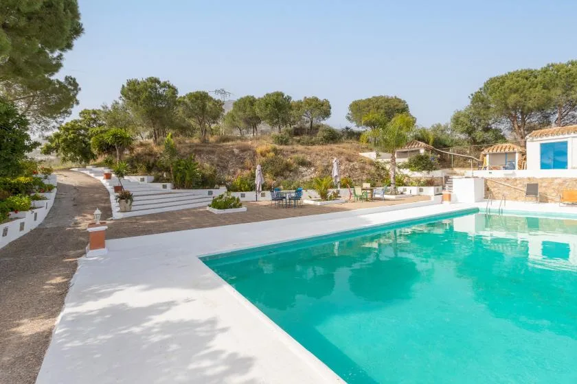 An outdoor swimming pool sits beside a paved terrace and landscaped grounds.
